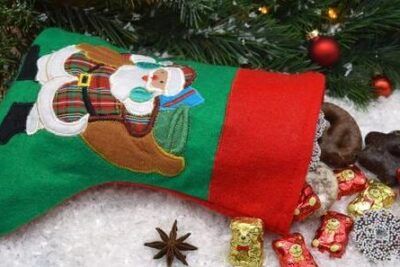 Calcetín navideño verde con Santa relleno de chocolates y dulces sobre nieve, significado de ponerse las botas explicacion y origen 1