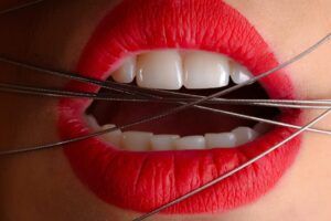 Primer plano de labios rojos y dientes blancos con cuerdas metálicas cruzadas, significado de sonar con caerse los dientes interpretacion y consejos 1