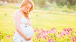 Mujer embarazada en vestido blanco sosteniendo su barriga en un campo de flores al atardecer significado de sonar con embarazo encuentra respuestas aqui