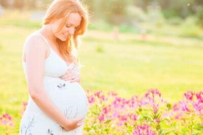 Mujer embarazada en vestido blanco sosteniendo su barriga en un campo de flores al atardecer significado de sonar con embarazo encuentra respuestas aqui