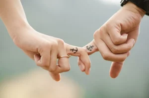 Dos manos entrelazando los meñiques con pequeños tatuajes de ancla en los dedos, significado de un tatuaje de ancla todo lo que necesitas saber.