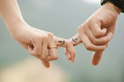 Dos manos entrelazando los meñiques con pequeños tatuajes de ancla en los dedos, significado de un tatuaje de ancla todo lo que necesitas saber.