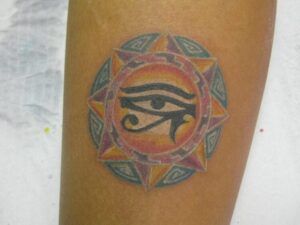 Tatuaje en antebrazo con un ojo central dentro de un sol geométrico de tonos naranjas, morados y azules, significado de un tatuaje de luna descubre su simbolismo.