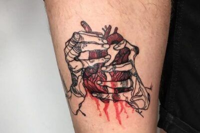 Tatuaje en muslo de manos esqueléticas que abren costillas mostrando un corazón anatómico sangrante significado del tatuaje de corazon roto descubre mas aqui