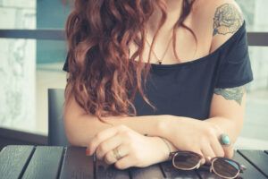 Mujer sentada con tatuajes florales visibles en el brazo y muñeca, significado del tatuaje de rosa en la muneca descubre su simbolismo.