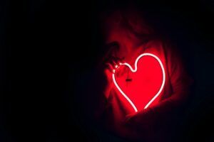 Corazón de neón rojo sostenido sobre el pecho que refleja el significado emoji amor.