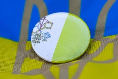 Pin redondo con dos llaves cruzadas sobre fondo blanco y verde colocado en una tela azul y amarilla con tridente, evocando el significado llave simbolo.