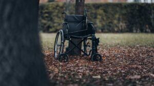 Silla de ruedas vacía apoyada contra un árbol sobre hojas otoñales que sugiere significado simbolismo rueda fortuna