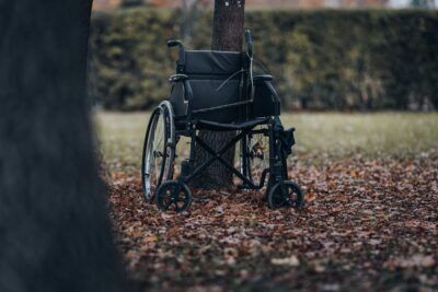 Silla de ruedas vacía apoyada contra un árbol sobre hojas otoñales que sugiere significado simbolismo rueda fortuna