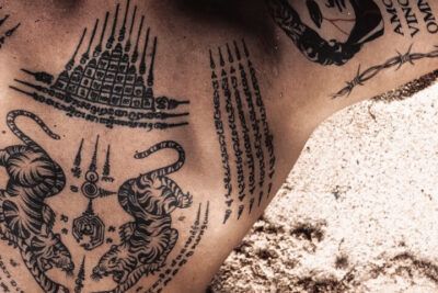 Significado y guia completa de un tatuaje de estrella en el pecho en una imagen de pecho decorado con tatuajes sak yant, dos tigres y líneas de escritura ritual