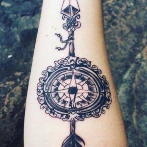 Tatuaje de flecha vertical con una brújula ornamentada en el antebrazo que refleja el significado y simbolismo de los tatuajes de flecha.