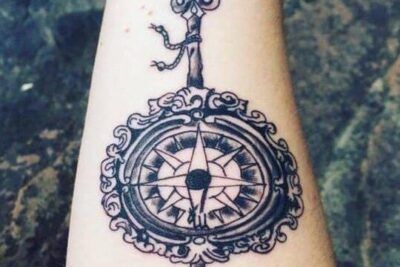Tatuaje de flecha vertical con una brújula ornamentada en el antebrazo que refleja el significado y simbolismo de los tatuajes de flecha.