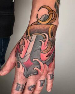 Tatuaje colorido en el dorso de la mano con motivos náuticos, formas onduladas y letras en los nudillos que acompaña el estudio sobre el significado y simbolismo de un tatuaje de cruz en el dedo 1