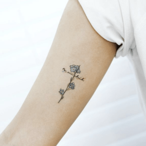 Tatuaje minimalista de línea fina con flores formando una cruz y caligrafía, relacionado con significado y simbolismo de un tatuaje de cruz en el pie