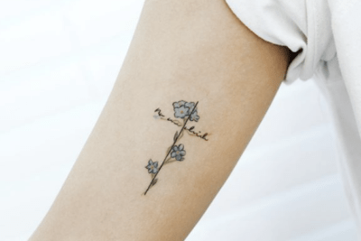Tatuaje minimalista de línea fina con flores formando una cruz y caligrafía, relacionado con significado y simbolismo de un tatuaje de cruz en el pie