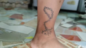 Rosario de cuentas con cruz en tinta negra sobre el tobillo que ilustra el significado y simbolismo de un tatuaje de cruz en el tobillo.