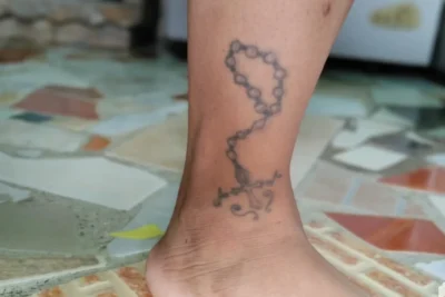 Rosario de cuentas con cruz en tinta negra sobre el tobillo que ilustra el significado y simbolismo de un tatuaje de cruz en el tobillo.