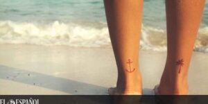 Piernas sobre la arena con tatuajes pequeños de ancla y palmera en los tobillos, imagen útil para explorar el significado y simbolismo de un tatuaje de cruz en la mano 1