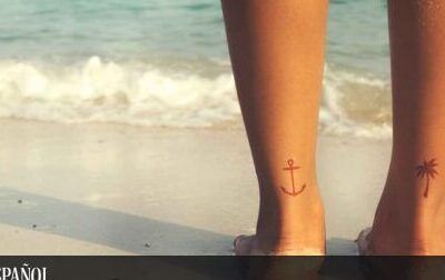 Piernas sobre la arena con tatuajes pequeños de ancla y palmera en los tobillos, imagen útil para explorar el significado y simbolismo de un tatuaje de cruz en la mano 1