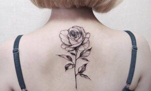 Rosa tatuada en tinta negra con sombreado y tallo vertical en la parte superior de la espalda, significado y simbolismo de un tatuaje de rosa 1