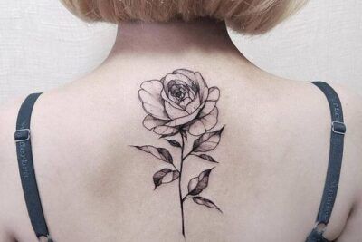 Rosa tatuada en tinta negra con sombreado y tallo vertical en la parte superior de la espalda, significado y simbolismo de un tatuaje de rosa 1