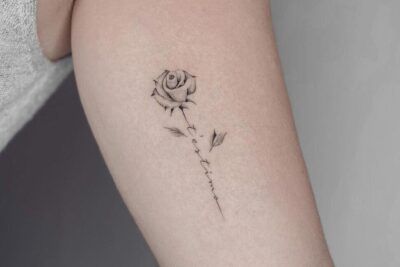Tatuaje minimalista en tinta negra de una rosa con tallo caligráfico que ilustra el significado y simbolismo de un tatuaje de rosa blanca.