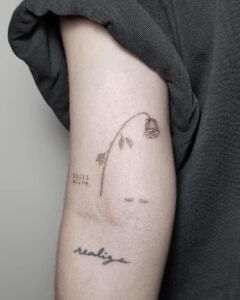 Tatuaje lineal en tinta negra de una rosa marchita y caída en el antebrazo que sugiere el significado y simbolismo de un tatuaje de rosa negra junto a pequeñas palabras tattoo.