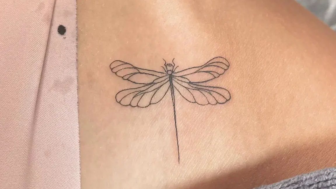 Tatuaje minimalista de libélula en el hombro que complementa el significado y simbolismo del tatuaje de rosa en el hombro