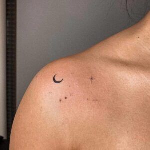 Tatuaje minimalista de media luna y pequeñas estrellas sobre la clavícula que evoca el simbolismo de un tatuaje de luna y estrella en el tobillo