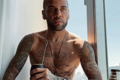 Hombre tatuado sin camiseta junto a una ventana, inspiración en el simbolismo del tatuaje de corazon con flecha en el cuello