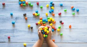 Manos infantiles sosteniendo caramelos multicolores sobre una mesa de madera, evocando simbolismo y caracteristicas del color purpura en la composición visual