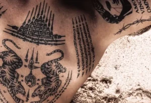 Tatuajes tradicionales Sak Yant en pecho y hombro con tigres y escrituras, evocando símbolos y útil para explorar simbolismo y significado de un tatuaje de angel en la mano