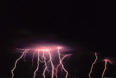 Relámpagos violetas descendiendo desde nubes oscuras, evocando sonar con un tsunami de lava significado y interpretacion