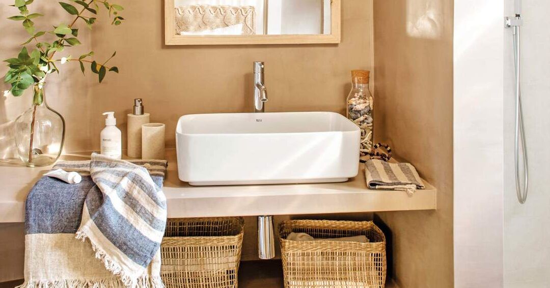 Lavabo rectangular blanco sobre encimera con grifo, toallas dobladas, cestas de mimbre y decoración natural, trucos para usar la escobilla del bano sin hacer ruido 1