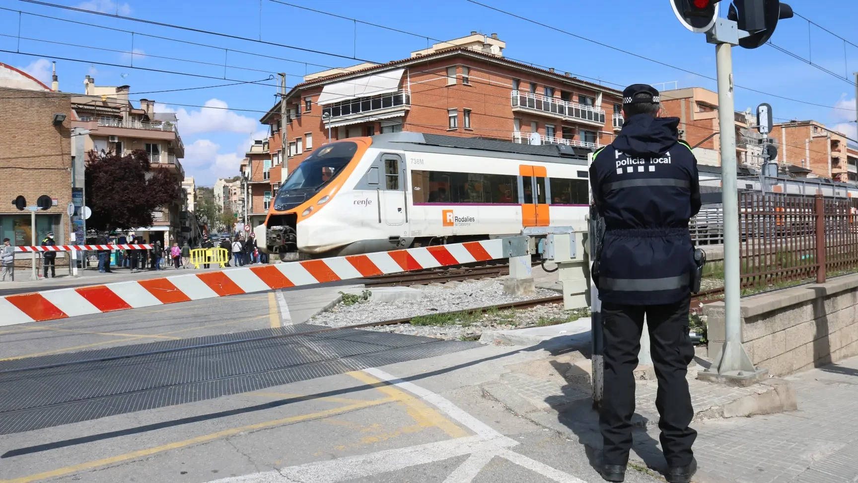Un agente controla un cruce ferroviario mientras un tren pasa, ilustrando un paso a nivel accesible para todos eliminando barreras en vias ferroviarias