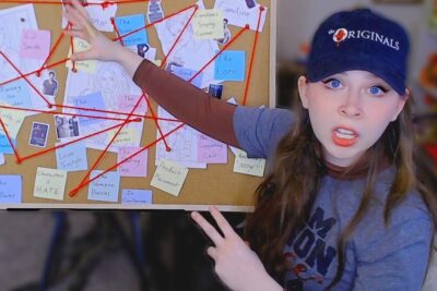 Persona señalando un tablero con hilos rojos y notas que conectan teorías sobre vampire diaries.