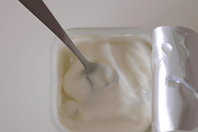 Envase abierto de yogur de soja con cuchara y textura cremosa; yogur de soja caducado es peligroso consumirlo